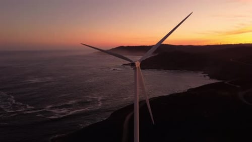 Aerial close up windmill wind turbine sunset with ocean cliff