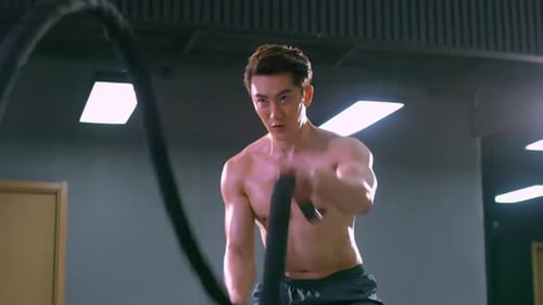 Athlete strong man in sport clothes doing battle ropes exercise workout at gym fitness