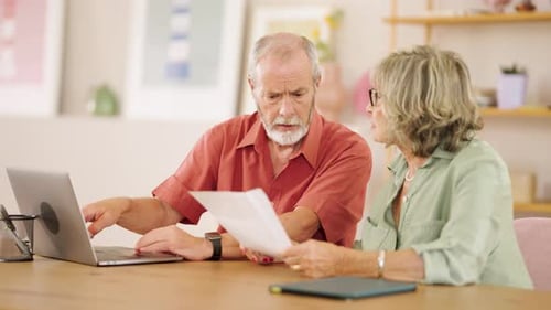 Senior Couple Examining Documents and Using Laptop at Home
