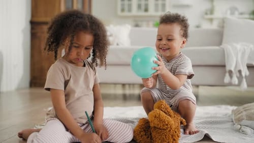Girl Drawing as Baby Brother Plays with Balloon