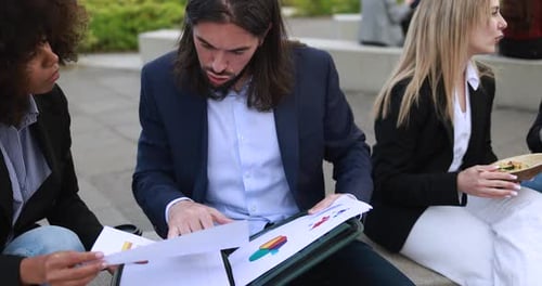 Multiracial business team analyses financial graphics over lunch in New York park