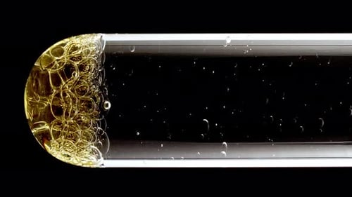 Makroaufnahme von unterschiedlich großen Goldblasen in absteigendem Glas im Reagenzglas auf schwarzem Hintergrund