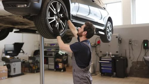 Mechanic Working on Tire of Elevated Car in Auto Repair Shop