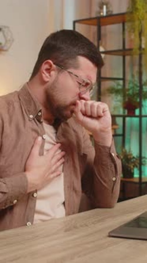 Man with Glasses Coughing Indoors While Using Laptop