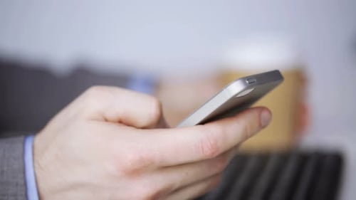 Businessman with smartphone drinking coffee in the office connecting with technology