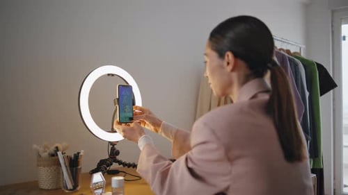 Jovencita concentrada ajustando el smartphone en un trípode preparando un vídeo tutorial en casa