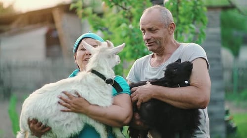 Cheerful Man and Woman Holding Kid Goats in Their Arms at the Farm