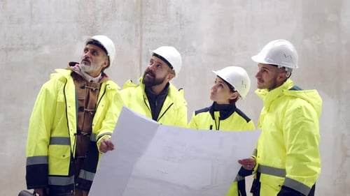 Construction Team Reviews Blueprint On Site Wearing Yellow