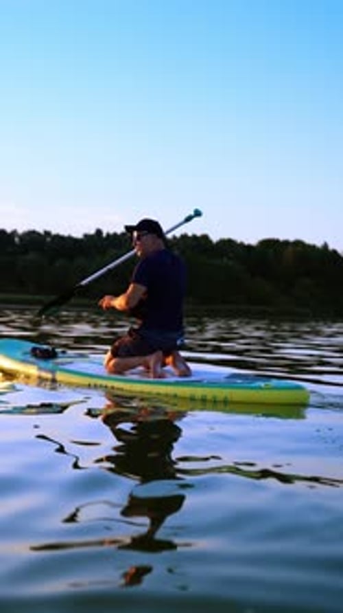 Sportsman kneeling on the inflatable sup board floats by the river.