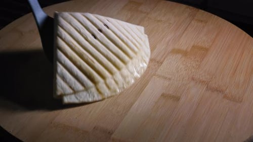 A close up shot of a freshly grilled Quesadilla being placed onto a cutting board, oil from the melt