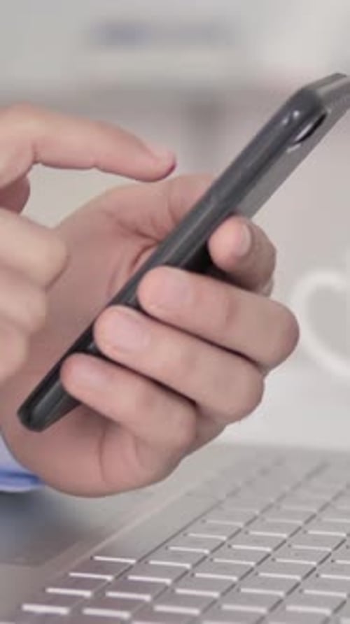 Man Using Smartphone Next to Laptop in Office
