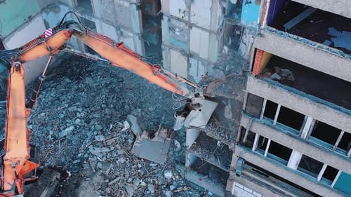 Excavator crashing floors of an old building and dusty debris falling down.