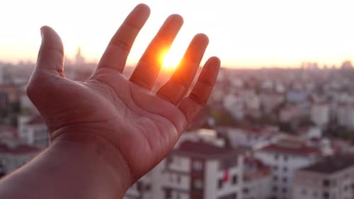 Hand Reaching for Sunset Over City Skyline