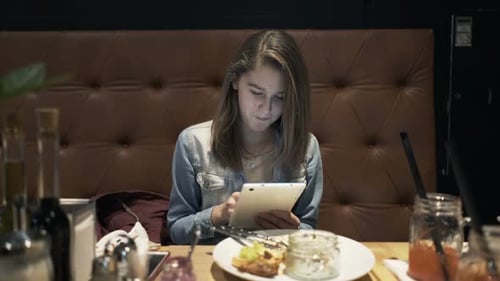 Teenage girl relaxes with tablet and meal at cafe table browsing the internet