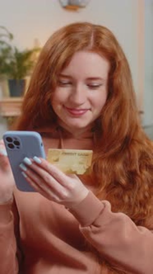 Happy Young Woman Using Credit Bank Card and Smartphone While Shopping Online Sitting on Sofa Couch