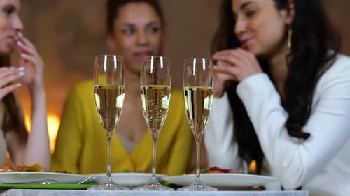 Moças felizes jantando em um restaurante e batendo taças com champanhe | Encontro de