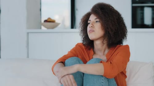 Woman Sitting on Couch Hugging Knees in Bright Room