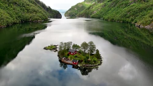 Small Island in a Lake with Red Houses Surrounded By Trees and Mountains in the Background