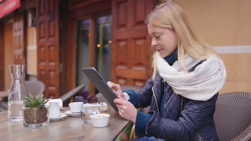 A Young Woman is Enjoying a Cup of Coffee While Using a Tablet at a Cozy Outdoor Cafe