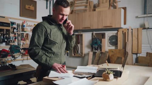 Man Using Phone and Laptop in Carpentry Workshop