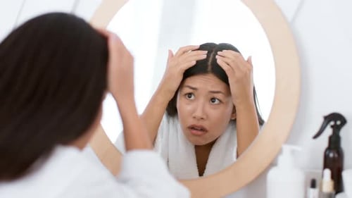 Worried Woman Examining Hair in Mirror at Home