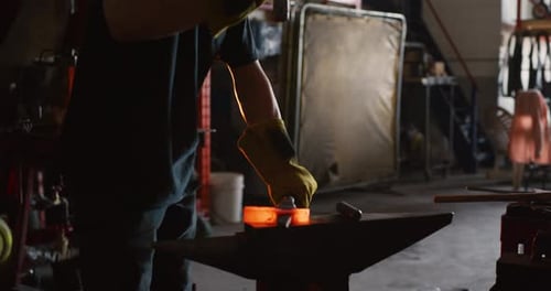 Professional blacksmith shapes red hot metal in dark workshop with hammer