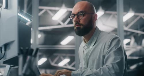 Bärtiger männlicher IT-Spezialist mit Brille, der sich intensiv auf den Computerbildschirm konzentriert