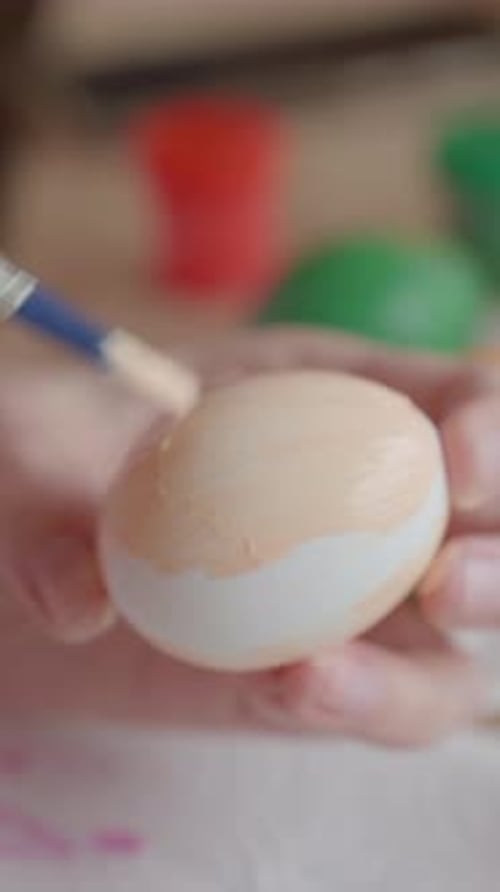 Woman painting Easter egg at home with pastel paints