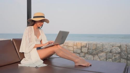 Glückliche Asiatin, die während der Reise, im Urlaub, im Urlaub einen Computer-Laptop am Strand benutzt