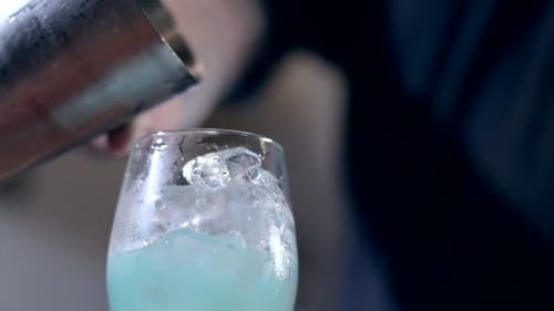 Bokeh shot of a bartender pouring a bright blue cocktail into a glass