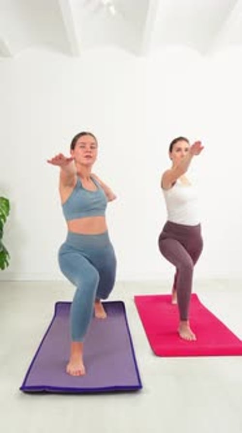 Two Young Women Practicing Yoga Poses in Studio