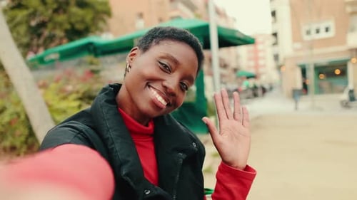 Happy young woman taking selfie on mobile phone sitting on bench on city street