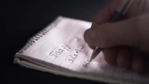 Hand writing shopping list on notepad for essentials close up shot