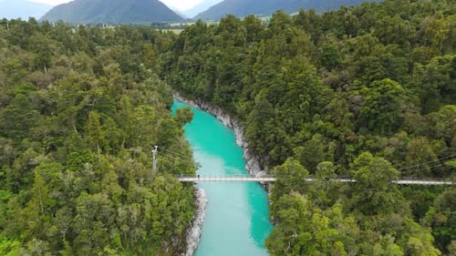 Aerial establishing shot of green dense forest landscape with Hokitika River, New Zealand. Mountain
