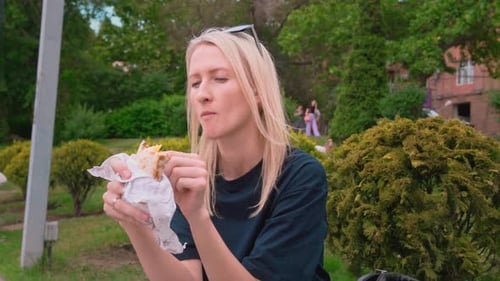 Close-up portrait of happy young blonde woman eating instant shawarma,