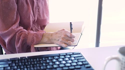 Caucasian businesswoman brainstorming ideas and writing in journal at office desk