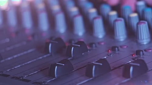 Sound Engineer Moves Faders Up and Down on Audio Mixer in Neon Light CloseUp