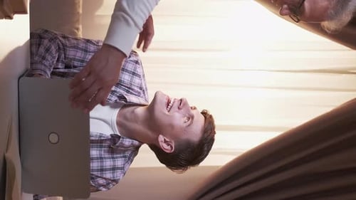Grandfather Helping Young Adult With Laptop at Desk