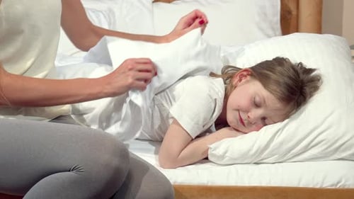 Tender Moment As a Mother Lovingly Tucks Her Little Daughter Into Bed