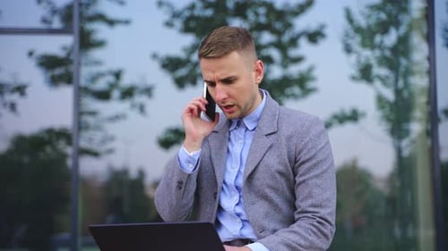 Young Man Talking on Phone with Laptop Outdoors