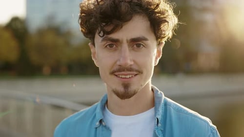 Nahaufnahmeporträt eines jungen gutaussehenden kaukasischen Mannes, der alleine draußen steht und lächelt und in die Kamera schaut