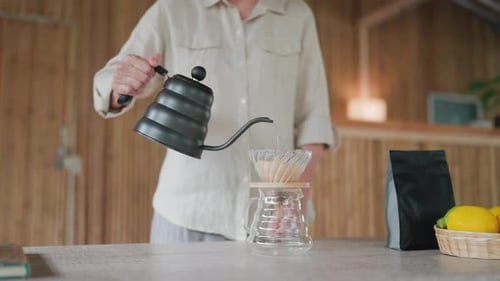 Close-up of an Asian elderly woman pouring hot water to make drip coffee in a bamboo house.