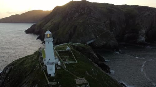 South Stack lighthouse aerial view passing island nautical landmark during golden hour sunrise