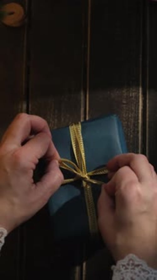 Hands Tying Gold Ribbon on Gift Box