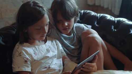 Two Focused Teen Age Children Girl and Boy Watching Content Together Indoors Using Tablet
