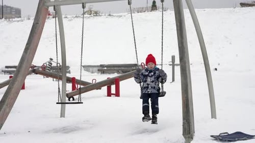Happy Child Swinging on a Playground in Winter Snow