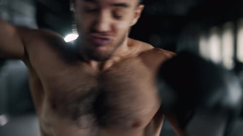 A Muscular Sportsman is Boxing in the Dark Gym