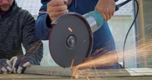 Close-up of construction workers using angle grinder, intense focus, sparks flying, metal cutting
