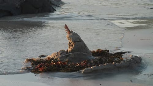Sandcastle at the beach getting hit by waves