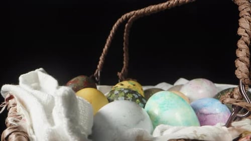 Ein Korb mit bemalten Eiern zu Ostern, der sich auf einem schwarzen Hintergrund dreht, und die Kamera zoomt langsam heran